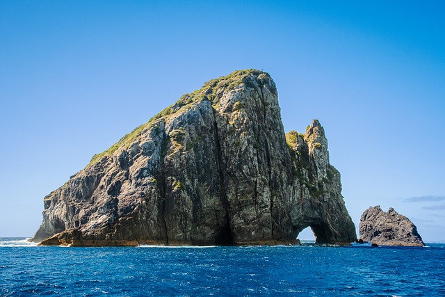 rock formation emerges from the sea, framed by the serene blue sky